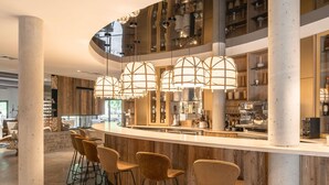 A modern bar area with a curved counter, multiple stools, and hanging pendant lights. - Hôtel Mercure Peyragudes Loudenvielle Pyrénées (Loudenvielle)