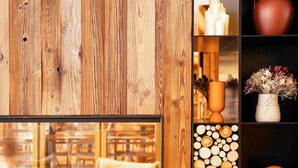 A wooden wall with a glass window, a fireplace with logs, and shelves with decorative items. - Hôtel Mercure Peyragudes Loudenvielle Pyrénées (Loudenvielle)