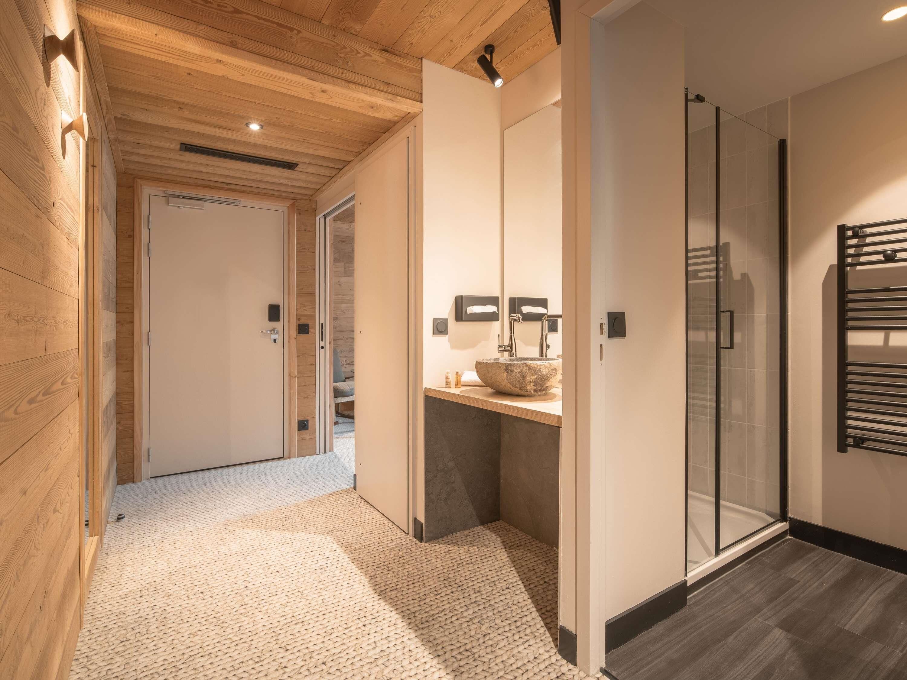 A modern bathroom with a glass shower enclosure, a wooden floor, and a sink with a stone basin.