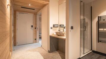 A modern bathroom with a glass shower enclosure, a wooden floor, and a sink with a stone basin.