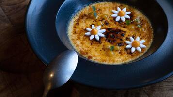Un tazón de sopa con una cuchara, adornado con flores, sobre un plato oscuro.