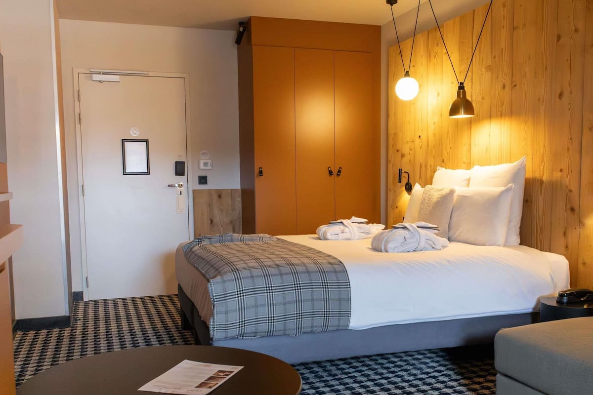 Une chambre d’hôtel avec un lit, une table ronde sur laquelle est posé un menu, une armoire en bois et un comptoir d’enregistrement.