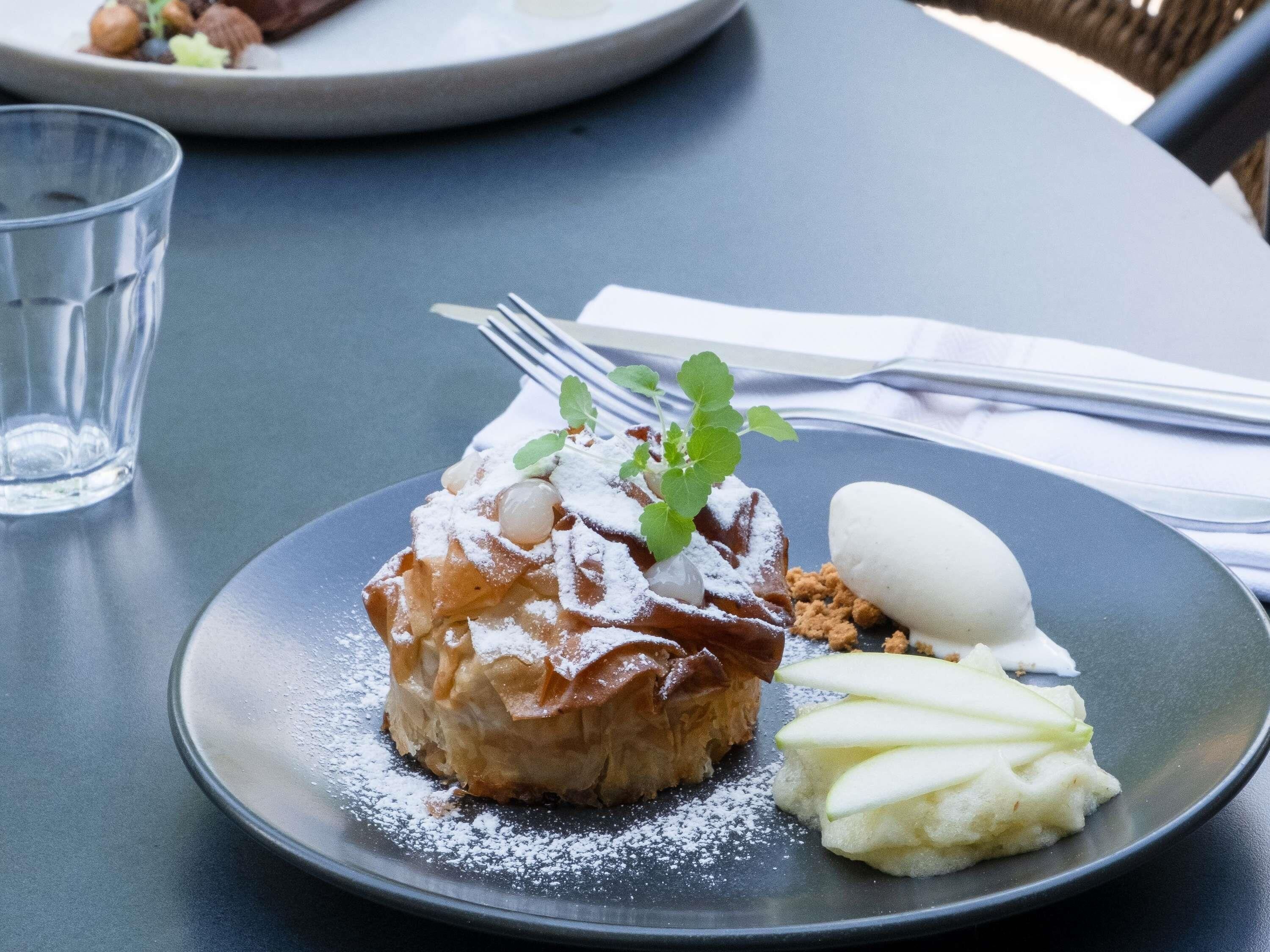 A dessert plate with a pastry, ice cream, and apple slices on a table.