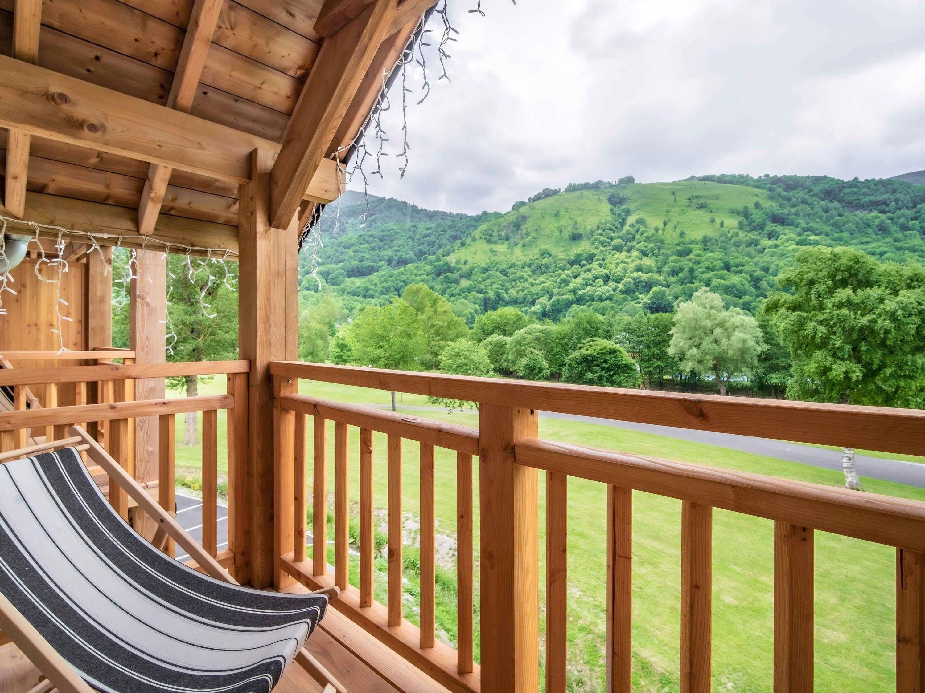 A wooden balcony with a hammock and a view of a green landscape.