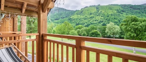 A wooden balcony with a hammock and a view of a green landscape.