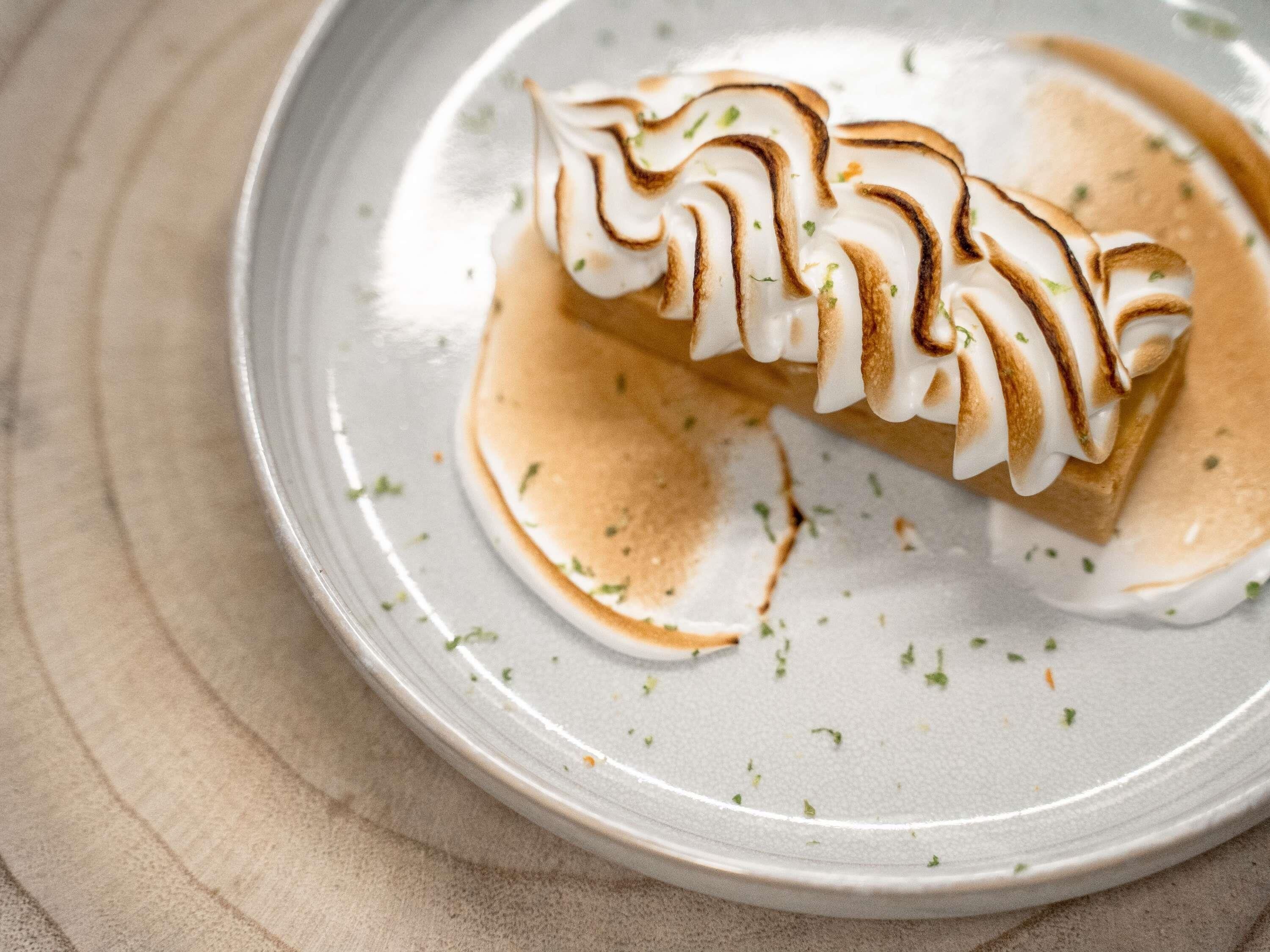 Un postre en un plato con cobertura cremosa y un hilo de salsa.