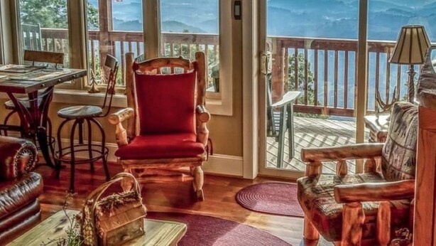 A cozy room with a wooden chair, a red sofa, and a view of mountains through large windows. - The Treetop Terrace, VIEWS, DECKS, SLEEPS 13 (West Jefferson)