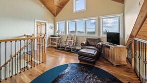 A spacious living room with a wooden ceiling, a leather sofa, a television, and a view through large windows. - The Treetop Terrace, VIEWS, DECKS, SLEEPS 13 (West Jefferson)