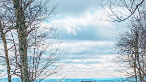 A two-story wooden cabin with a snow-covered roof, surrounded by trees and a mountainous landscape. - The Treetop Terrace, VIEWS, DECKS, SLEEPS 13 (West Jefferson)