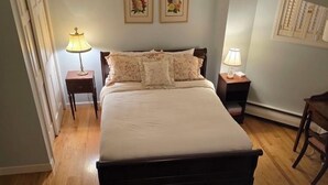 Um quarto com uma cama grande, duas luminárias de cabeceira, uma cadeira de madeira e duas fotos emolduradas com flores na parede.