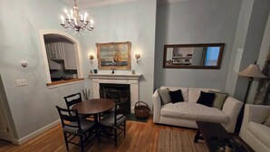 Uma sala de estar com lareira, uma mesa de jantar com cadeiras, um sofá e um lustre.