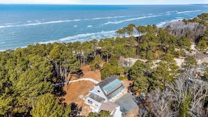An aerial view of a coastal property with a house surrounded by dense forest, overlooking the ocean.