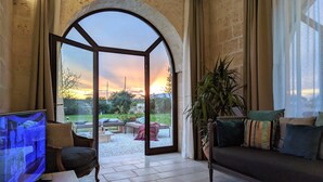 A spacious living room with a large arched window, a comfortable sofa, a television, and a potted plant. - Trullo Don Mino, near Alberobello and Locorotondo, private pool (Locorotondo)