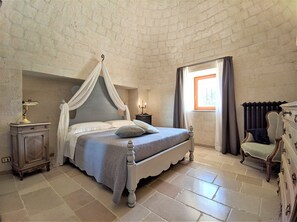A bedroom with a four-poster bed, a nightstand with a lamp, a dresser, and a window with curtains. - Trullo Don Mino, near Alberobello and Locorotondo, private pool (Locorotondo)