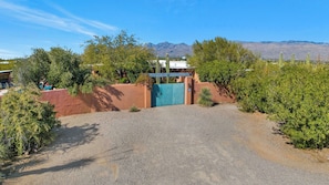 A gated entrance with a gravel driveway leading to a building with a blue door. - Saguaro Retreat-Salt Pool, Spa, Mountain Views (Tucson)