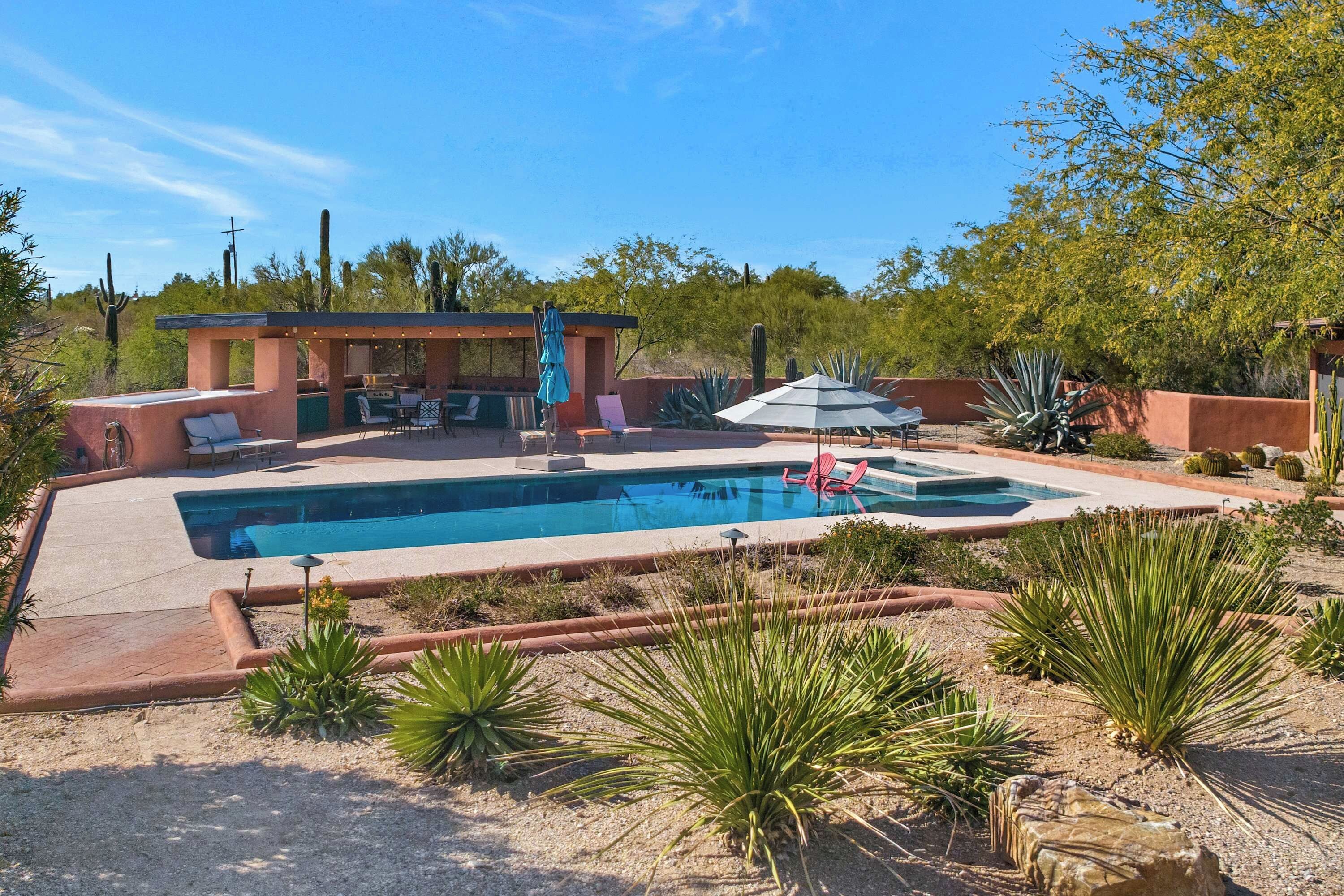 Un patio trasero con piscina, mobiliario exterior y cactus.