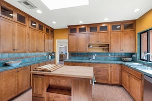 A kitchen with wooden cabinets, a central island, and a backsplash with blue tiles. - Saguaro Retreat-Salt Pool, Spa, Mountain Views (Tucson)