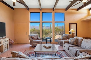 A spacious living room with a large window, leather sofas, a coffee table, and a television. - Saguaro Retreat-Salt Pool, Spa, Mountain Views (Tucson)