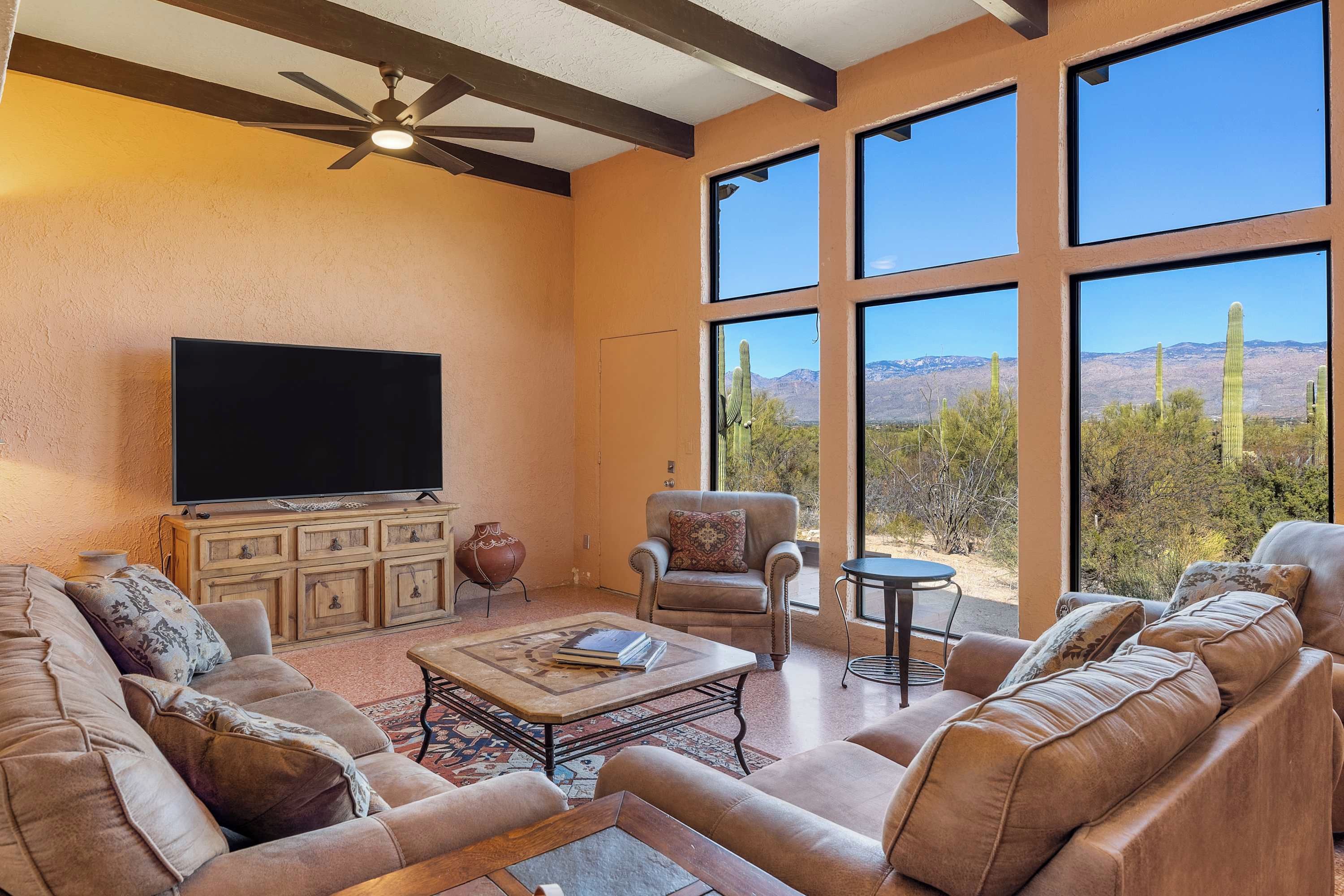 A spacious living room with a large flat-screen TV, leather sofas, a coffee table, and a ceiling fan.