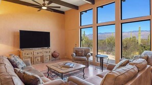 Una sala de estar con un televisor grande, sofás de cuero, una mesa de centro y vistas a cactus y montañas a través de amplias ventanas.