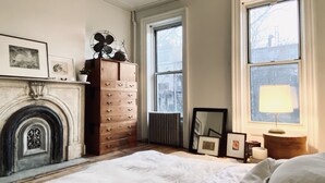 Un dormitorio con chimenea, cómoda, cama y ventanas grandes.