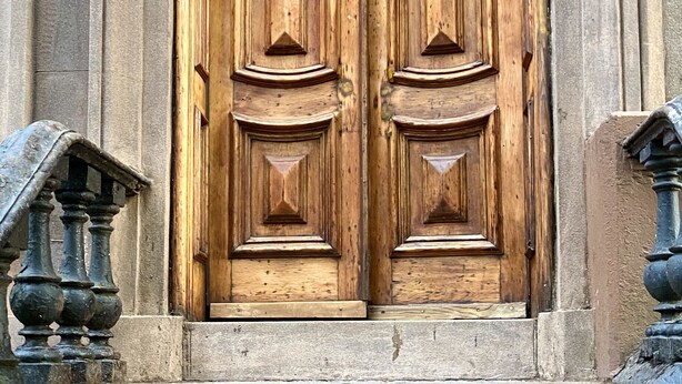 Una puerta doble de madera grande con un accesorio de luz encima, ubicada en un edificio de piedra.