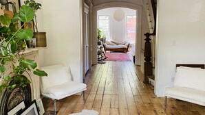 Un pasillo con sofás blancos, piso de madera y vista a una habitación con una silla y un ventilador.
