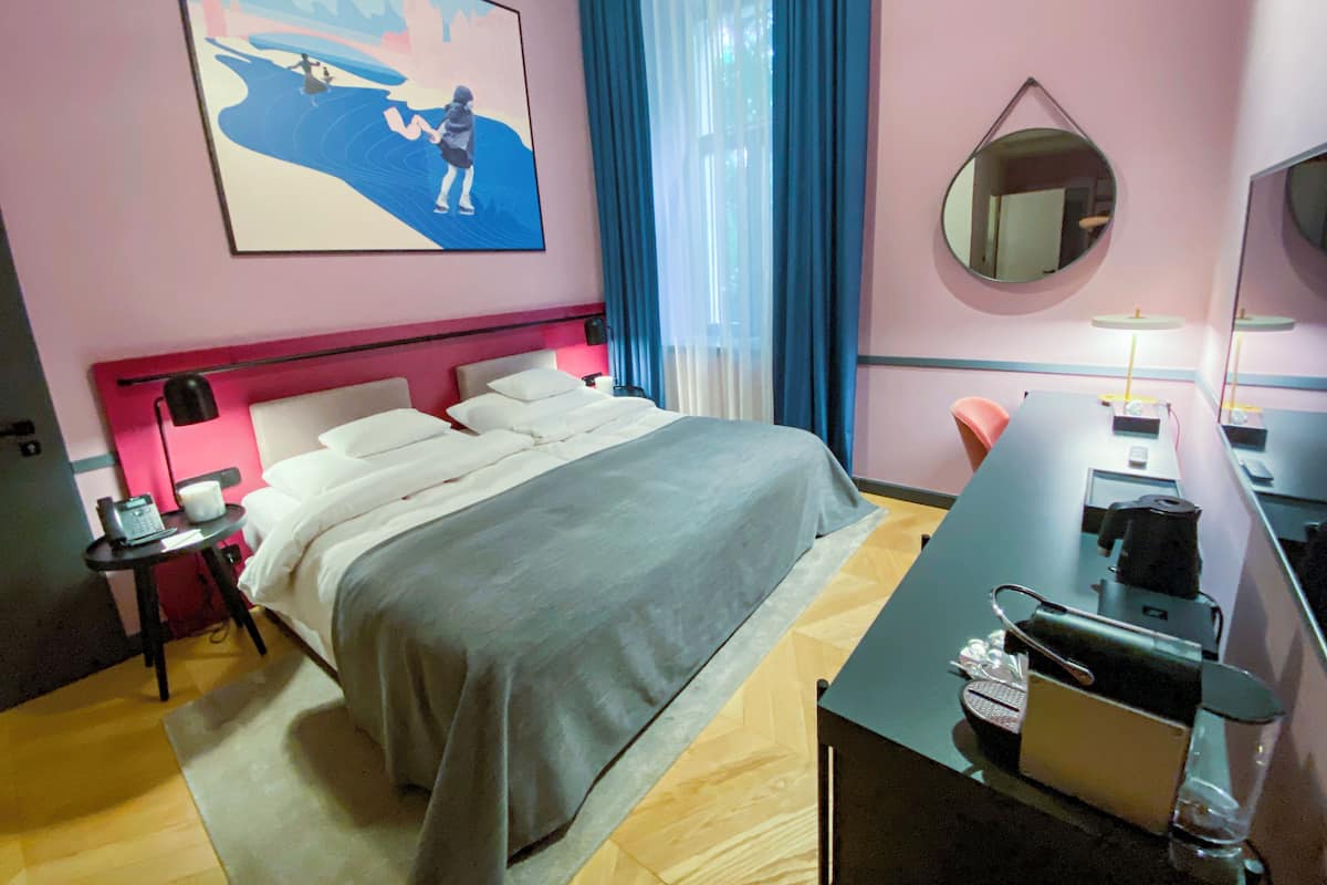 Una habitación de hotel con una cama, un escritorio con computadora, teléfono y espejo.