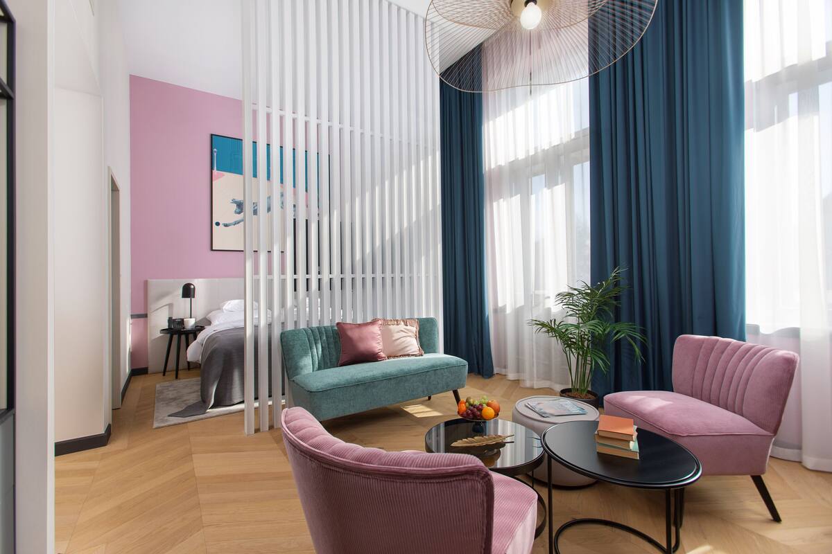 Una sala de estar moderna con un sofá azul verdoso, un sillón rosa y una mesa de centro con libros y fruta.
