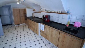 A kitchen with wooden cabinets, a black countertop, a sink, and a tiled floor. - RefuKium 'Alte Brennerei' in the center of Weißenburg (Weißenburg in Bayern)
