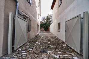 Une ruelle étroite, pavée de pierres et bordée de portails en métal de part et d’autre.