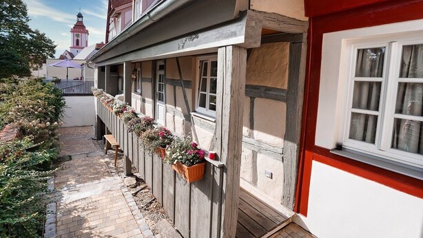 A narrow alleyway with a building featuring a red and white facade, wooden beams, and flower boxes on the exterior wall. - RefuKium 'Alte Brennerei' in the center of Weißenburg (Weißenburg in Bayern)