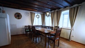 A dining room with a wooden table and chairs, a clock on the wall, and a window with curtains. - RefuKium 'Alte Brennerei' in the center of Weißenburg (Weißenburg in Bayern)