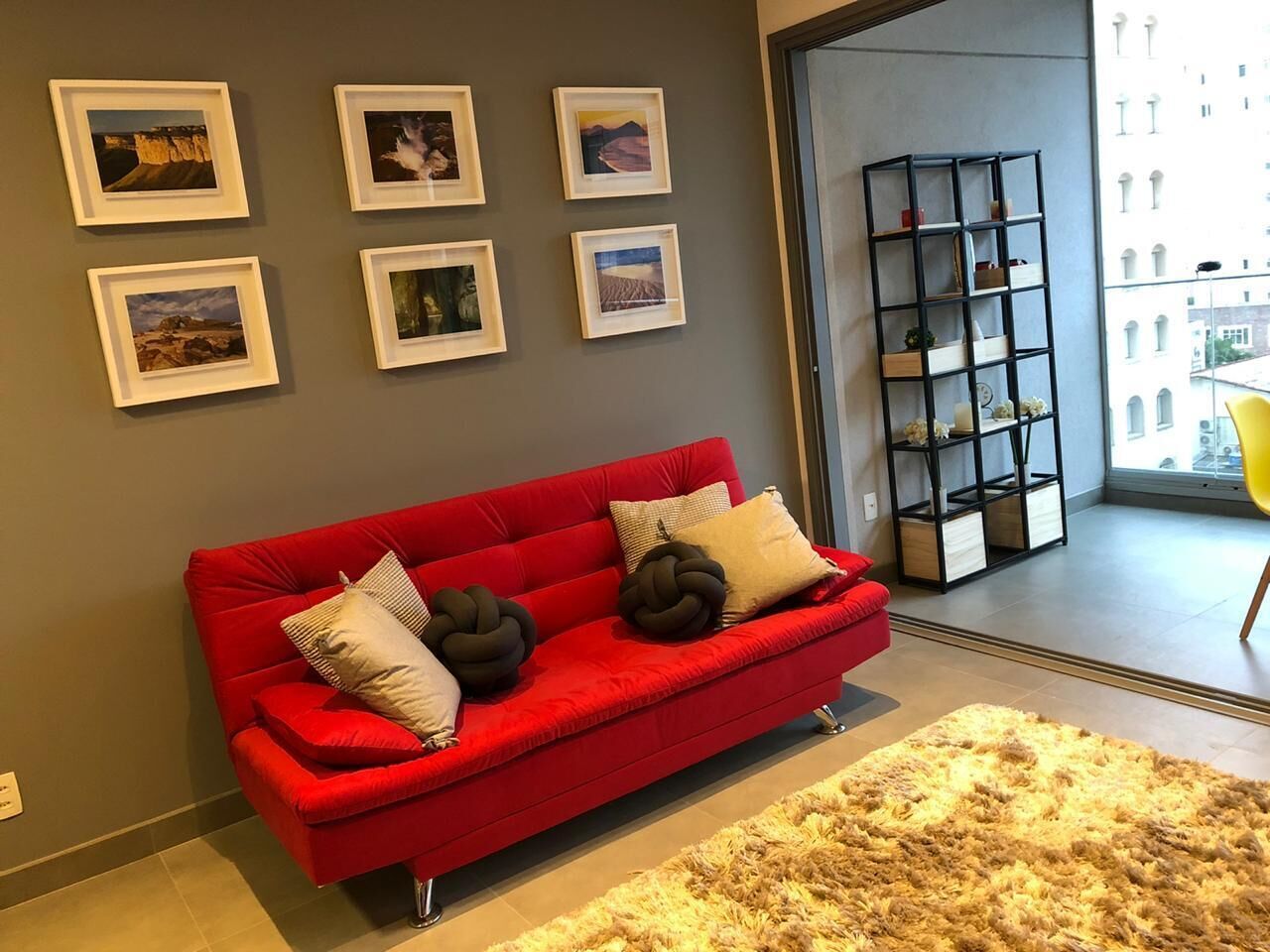 A red sofa with decorative pillows, a fluffy rug, and framed pictures on the wall.