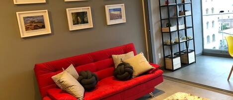 A red sofa with decorative pillows, a fluffy rug, and framed pictures on the wall.