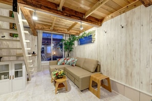 Relax in this inviting living area with a sofa, stool, and side table, surrounded by a staircase and a large window.