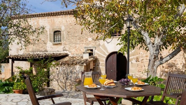 An outdoor dining area with a rustic stone table, wooden chairs, and a stone wall in the background. - Finca Morro, in a quiet location, views of the mountains, pool, WIFI, A/C (Pollenca)