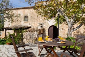 Un área de comedor al aire libre con una mesa de piedra rústica, sillas de madera y un muro de piedra al fondo.