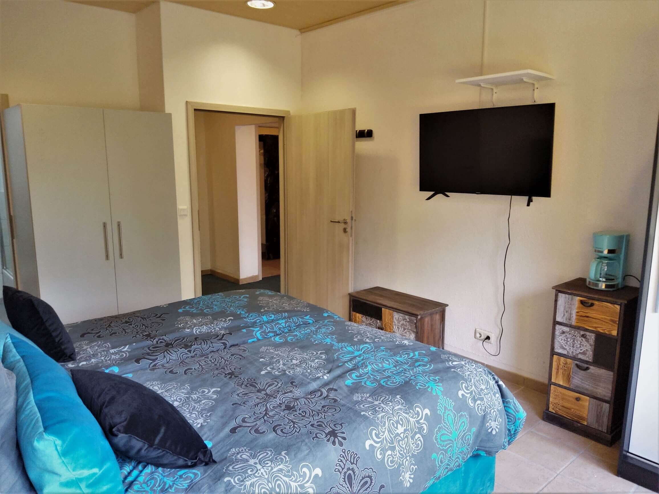 A bedroom with a bed, wardrobe, television, and a coffee maker.