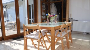 A dining area with a glass-top table, wooden chairs, and a view through large glass doors to an outdoor patio.
