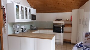 A kitchen with white cabinets, a microwave, an oven, a fan, and a coffee maker.