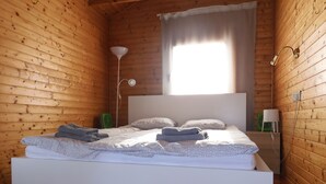 A modern wooden room with a bed, a standing fan, and a window with curtains.