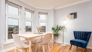 A modern dining area with a wooden table and white chairs, large windows, and a blue chair.