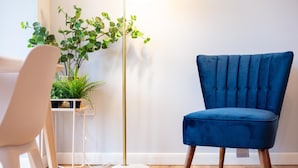 A blue chair, a white chair, and a floor lamp with a plant beside it.