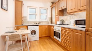 A compact kitchen with wooden cabinets, a washing machine, a microwave, and a sink.