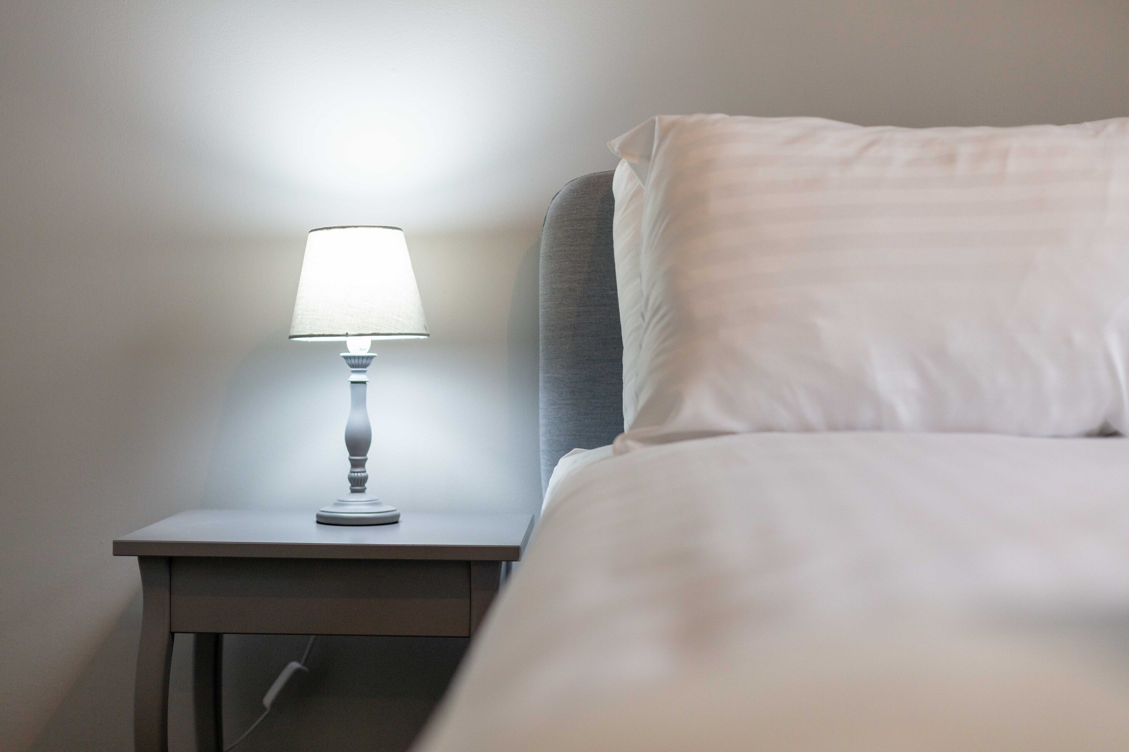 A neatly made bed with a white pillow and a bedside table with a lamp.