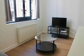 Una habitación con una mesa redonda de vidrio, un mueble bajo para televisor negro y un ventanal con cortinas.