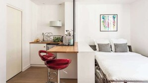 A modern room with a bed, a small kitchenette, and a red chair. - Newly Renovated, Modern Studio Flat in Montmartre (Paris)