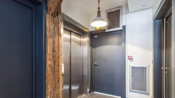 A hallway with two elevators, a wooden accent wall, a ceiling light, and a vent. - Newly Renovated, Modern Studio Flat in Montmartre (Paris)