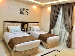 A hotel room with two beds, a nightstand, a lamp, and a painting on the wall. - Jewel Dokki Hotel (Giza)